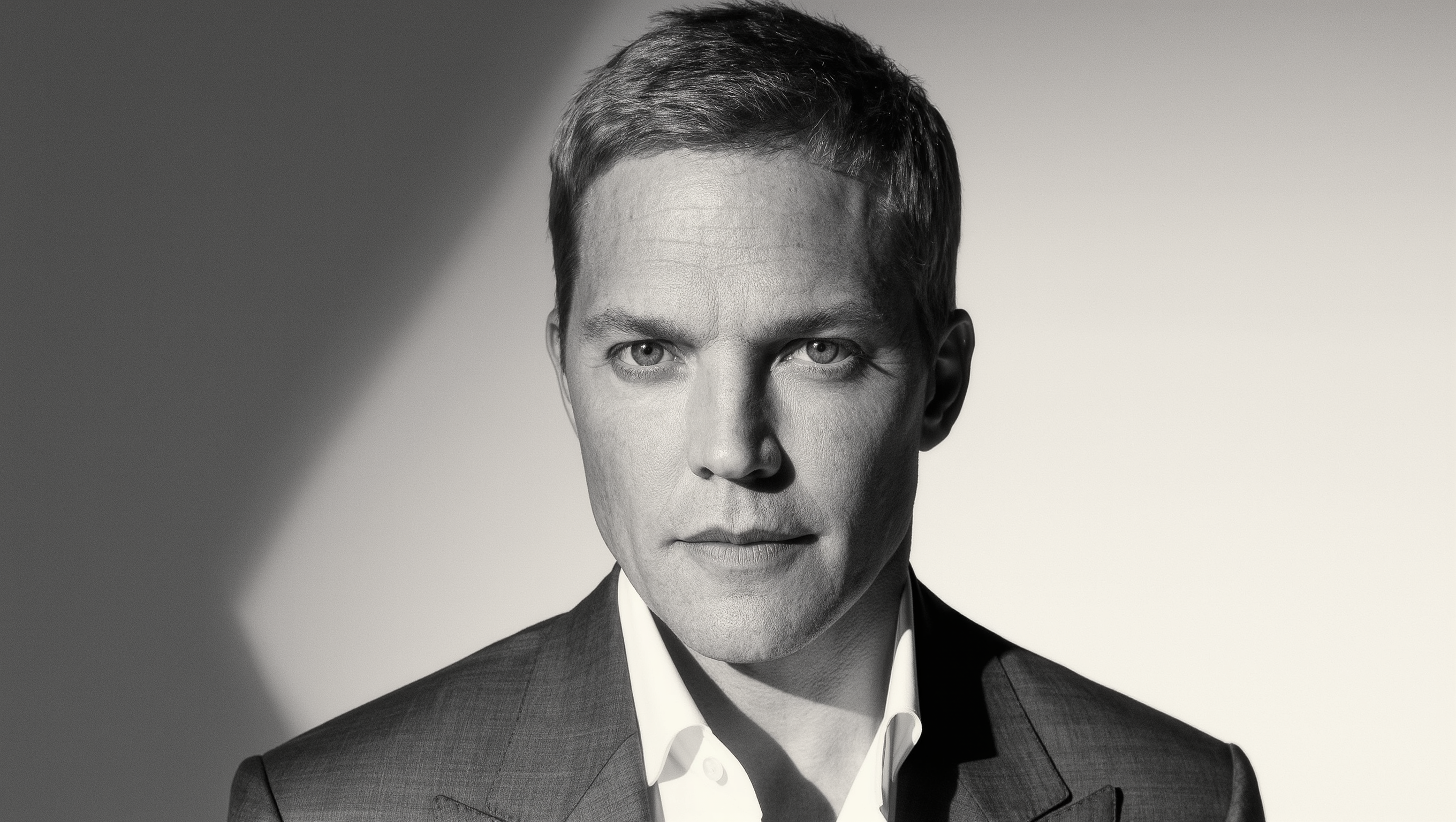 Monochrome editorial portrait of a man in formal styling and sharp studio light.