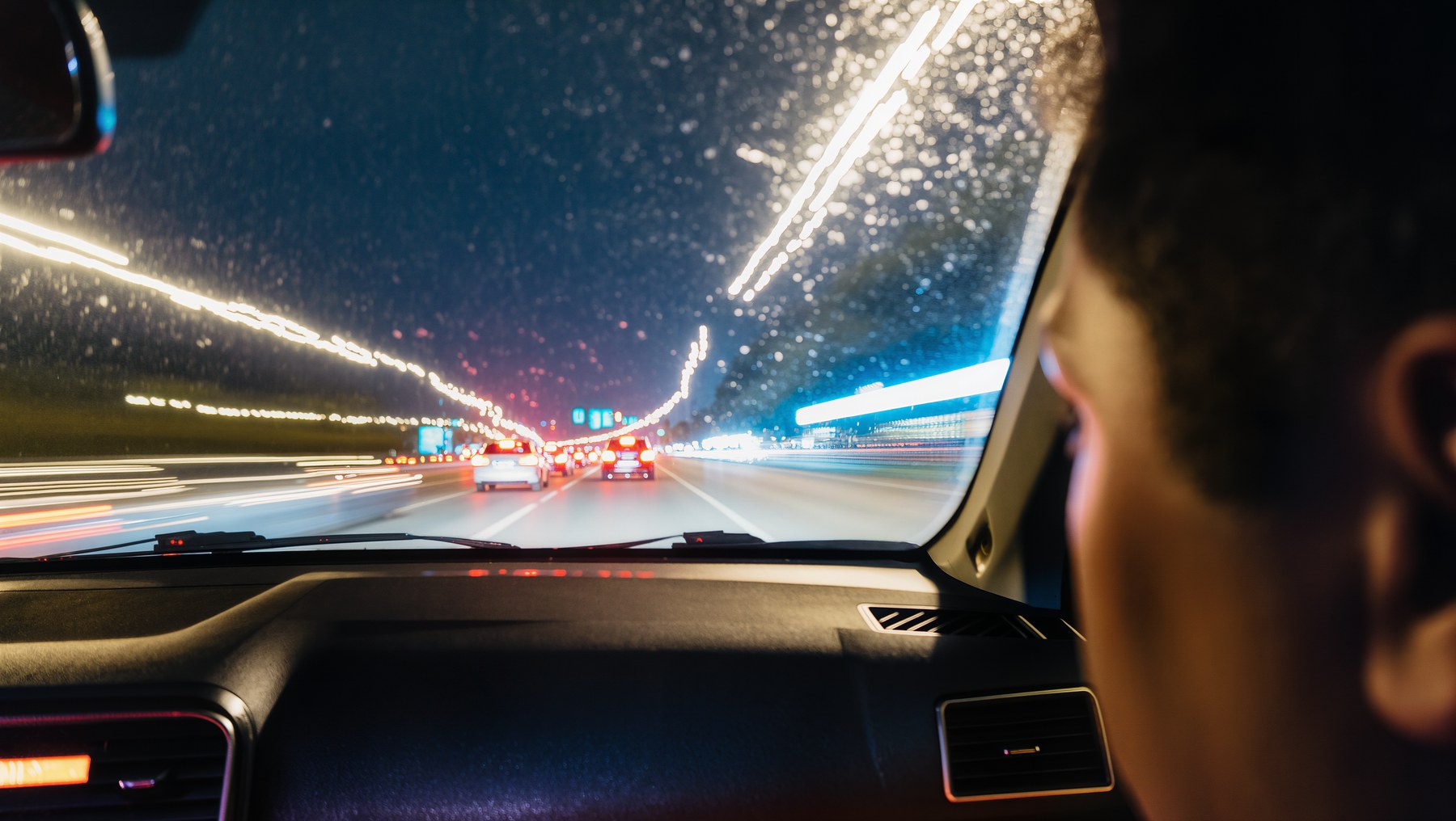 Night driving view through a rain-covered windshield.